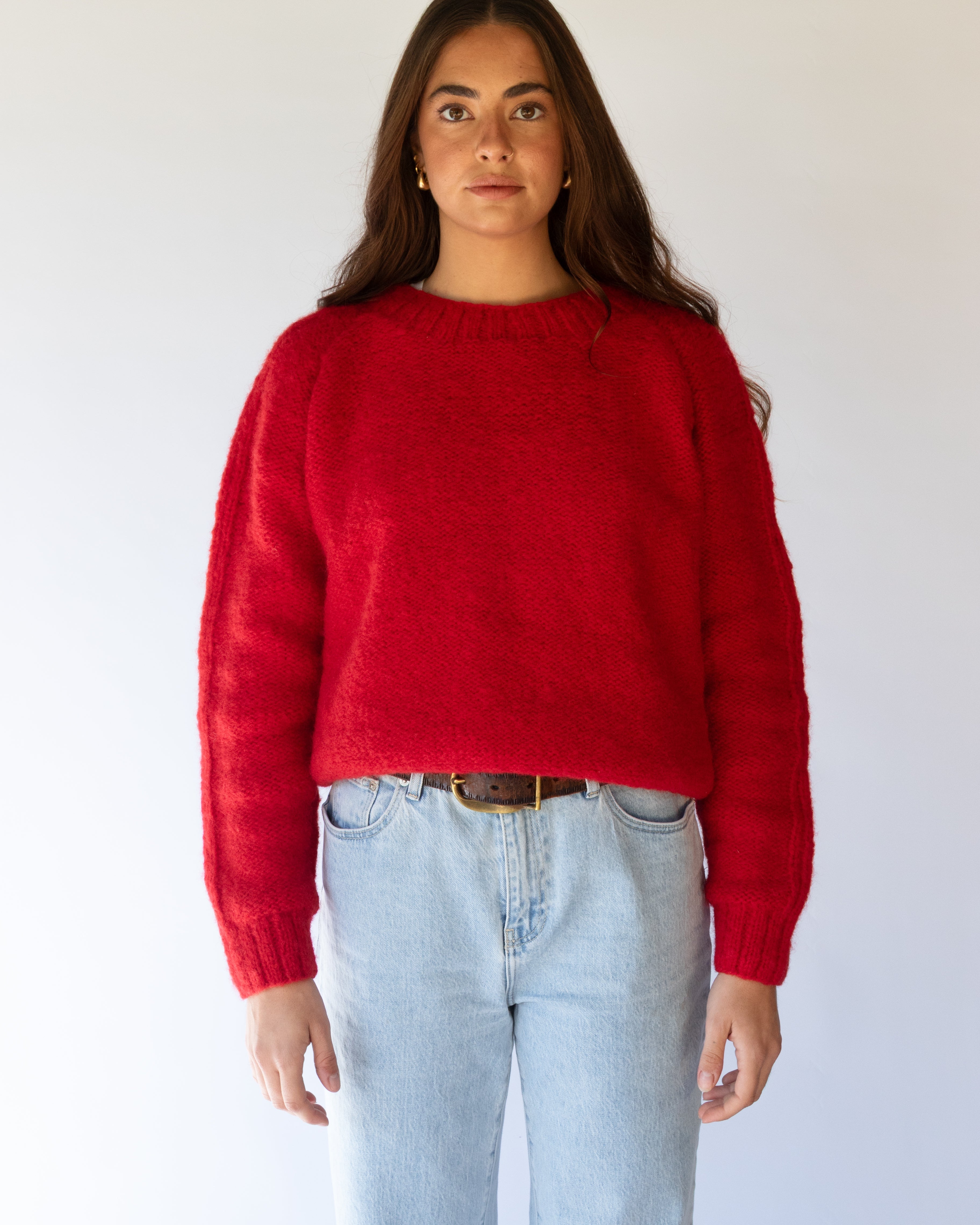 Person wearing a red sweater and light blue jeans against a white background