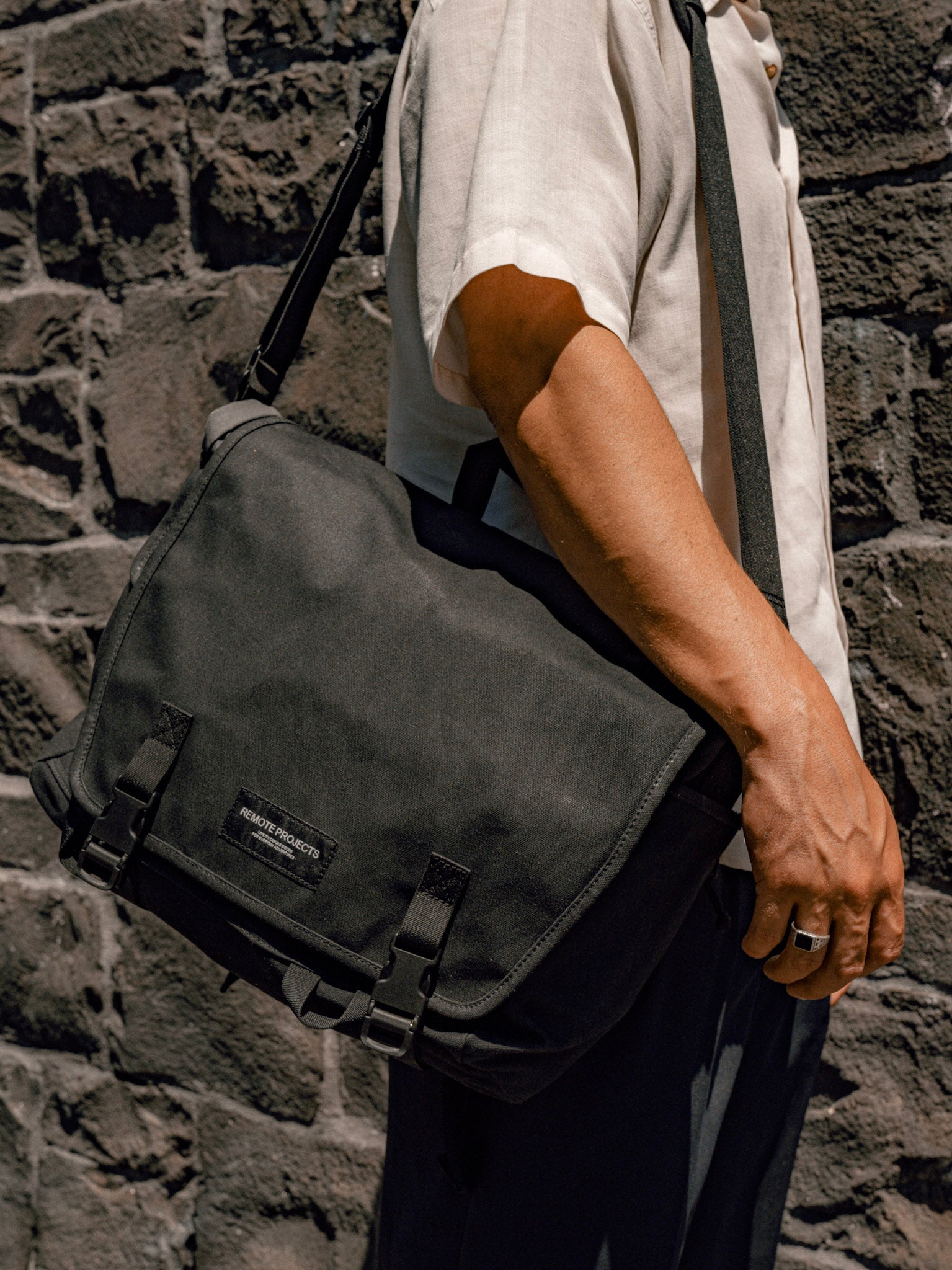 Person holding a black messenger bag against a stone wall