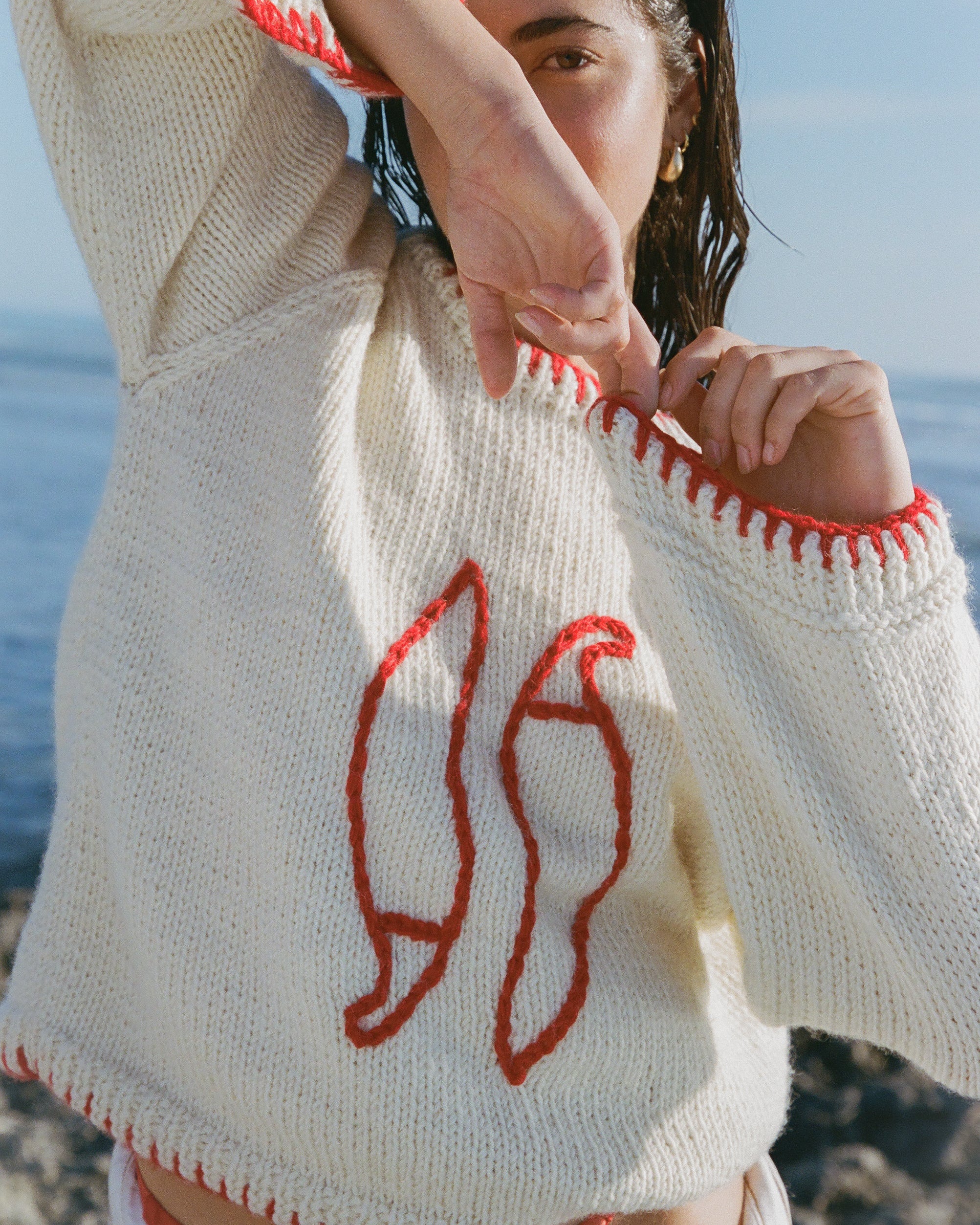 Person wearing a cream sweater with red patterns by the ocean