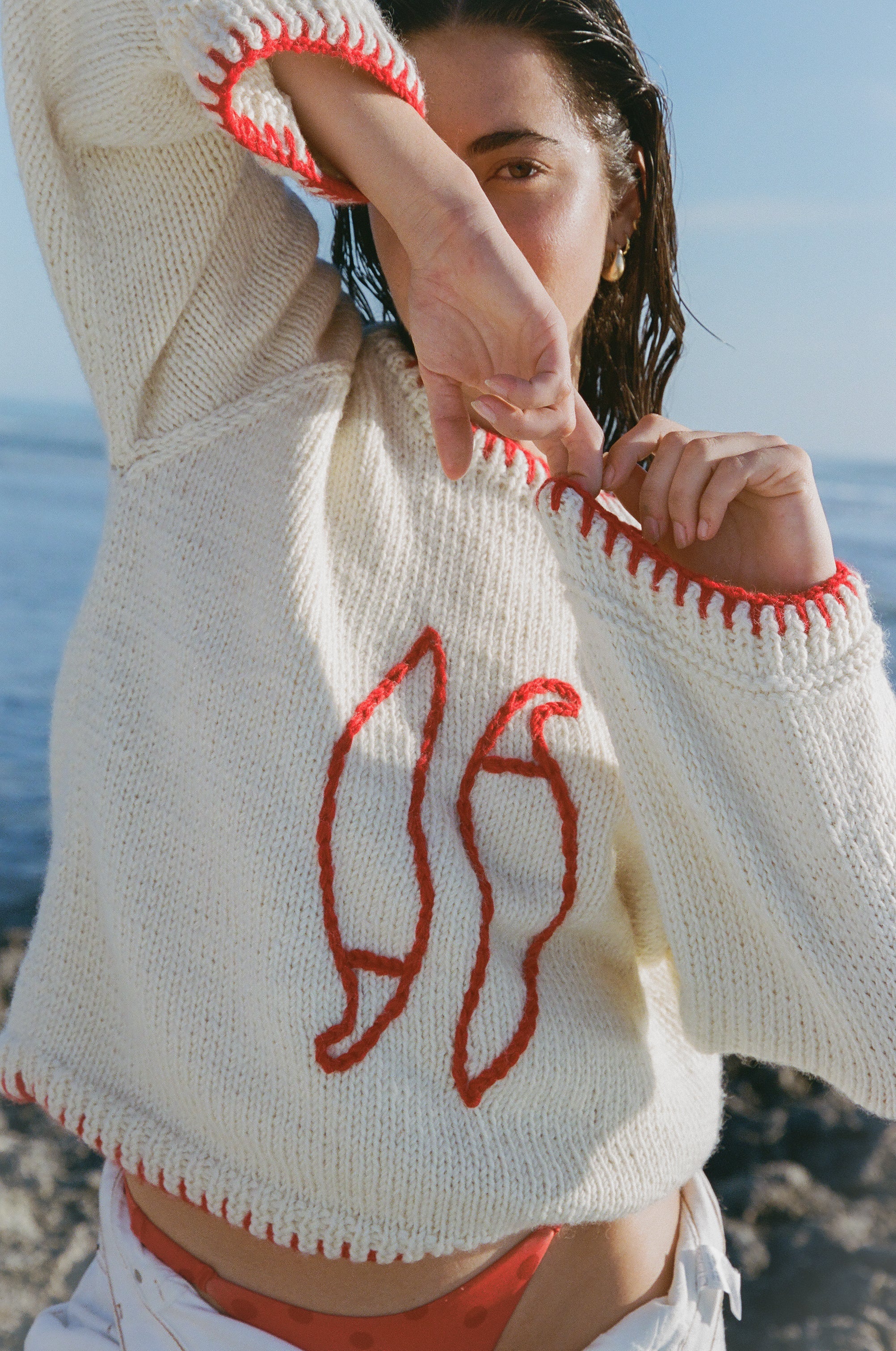 Person wearing a cream sweater with red patterns by the ocean