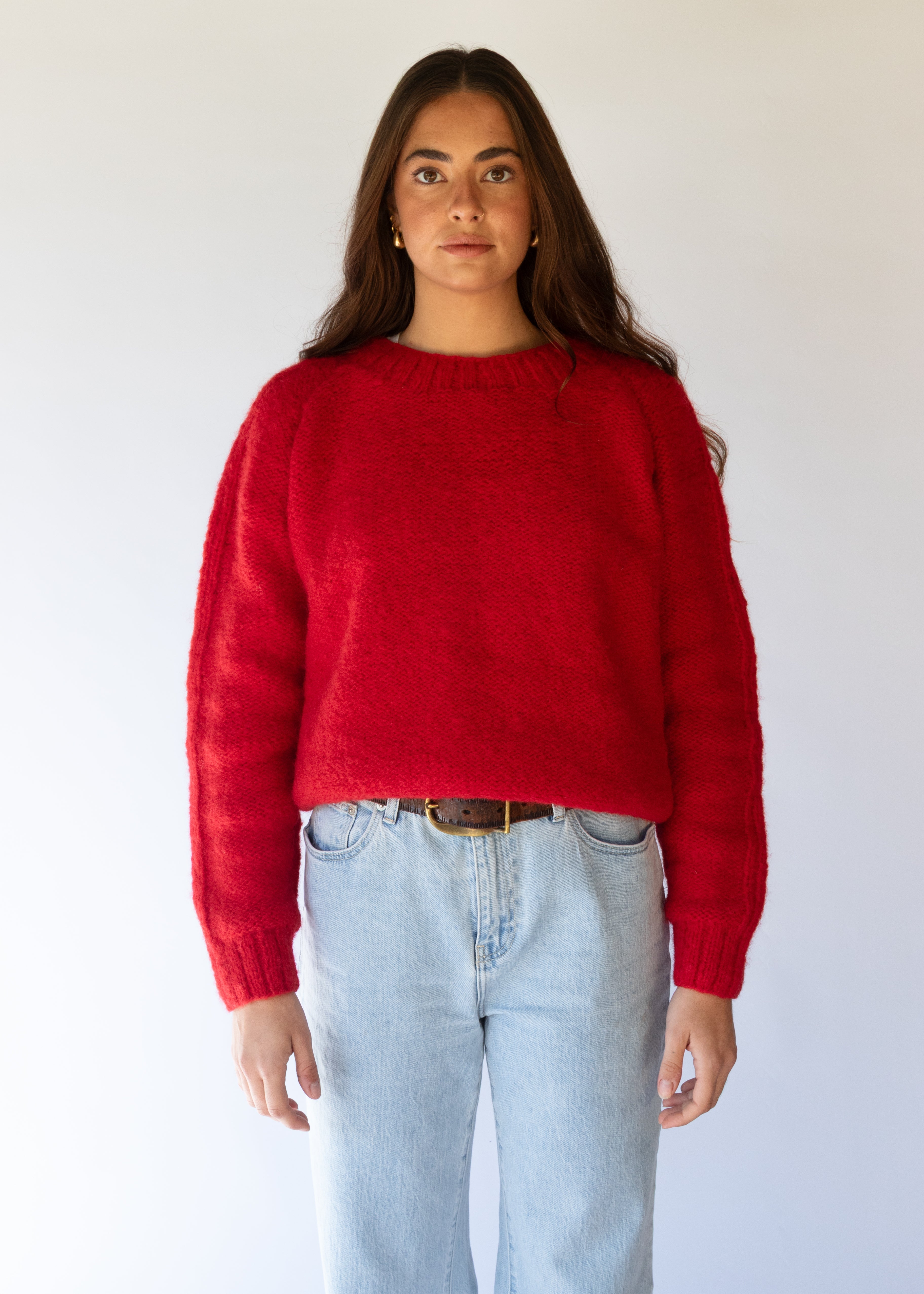 Person wearing a red sweater and light blue jeans against a white background