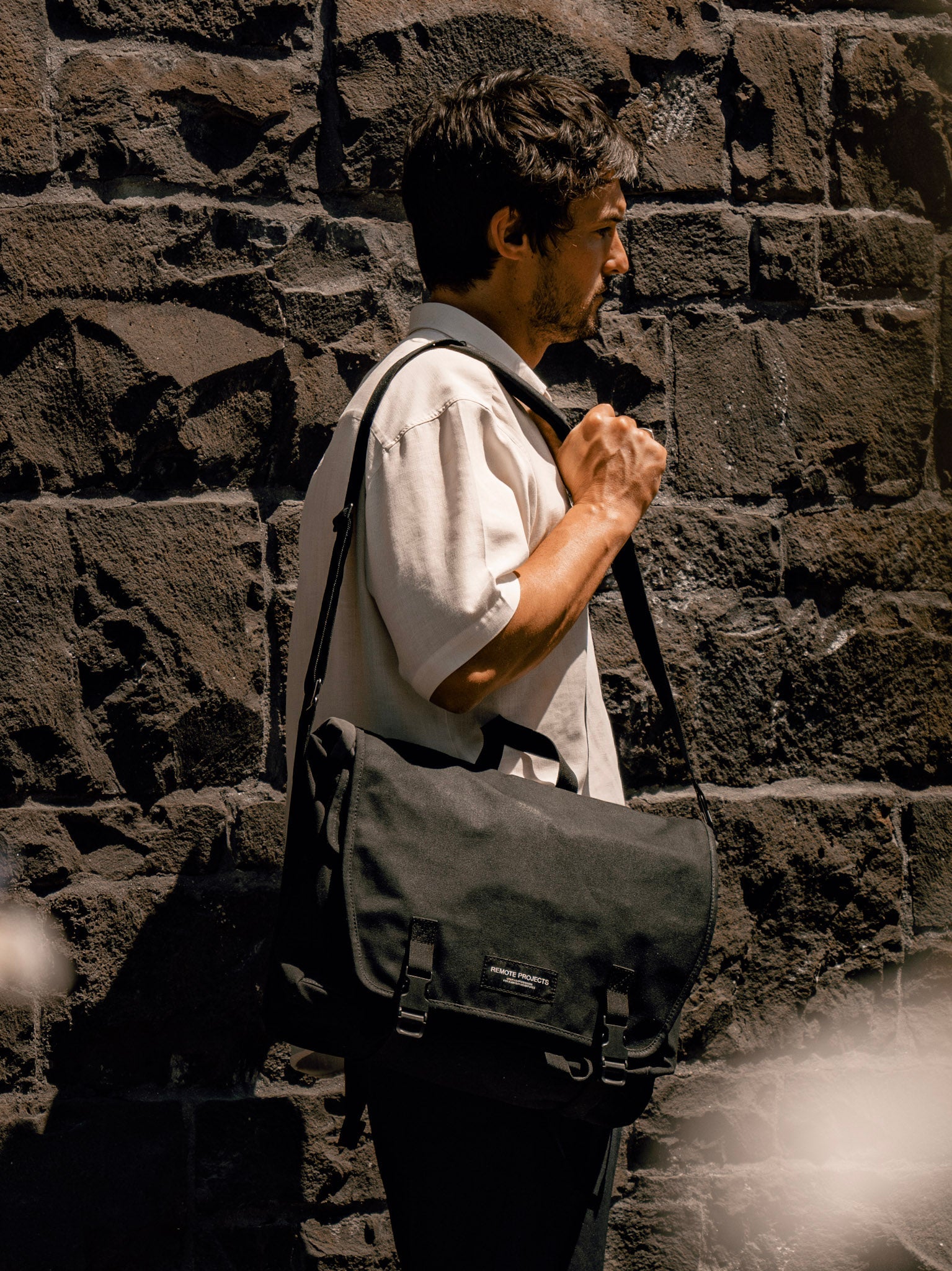 Man with a gray shoulder bag against a stone wall